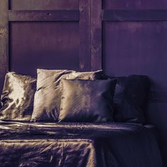 a bed topped with lots of pillows next to a purple wall and wooden door behind it