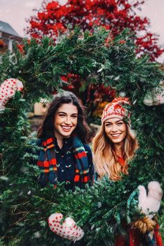 two women standing in front of christmas wreaths with red and green decorations on them