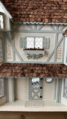 a white doll house with brown shingles on the roof and windows in front of it