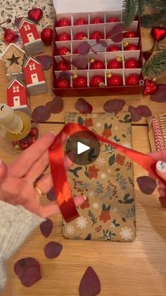 a person cutting a red ribbon on top of a wooden table next to christmas decorations