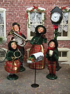 three dolls are posed in front of a brick wall with a clock and musical instruments