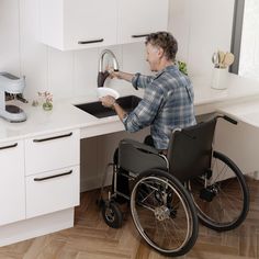 a man in a wheelchair is washing dishes at the kitchen sink with his hands on the faucet