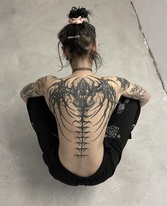 a woman sitting on the ground with her back to the camera and tattoos on her body