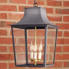 a lantern hanging from the side of a brick wall with three lit candles in it