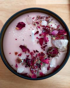 a bowl filled with pink liquid and flowers on top of a wooden table next to a candle