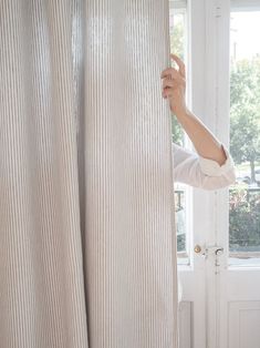 a woman peeking out from behind a curtain with her hand on the window sill