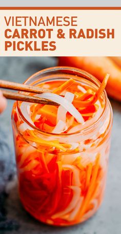 a person holding chopsticks over a jar filled with carrots and other vegetables