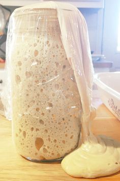 a glass jar filled with white liquid sitting on top of a wooden table next to a spoon