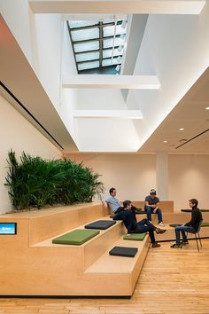 four people sitting on benches in an office lobby with plants growing out of the ceiling