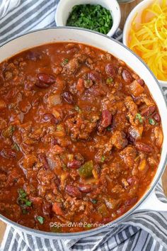 a large pot filled with chili and cheese next to other food on a wooden table