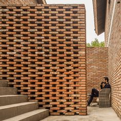 a man sitting on a chair in front of a brick building with stairs leading up to it