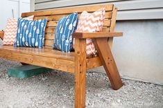 a wooden bench with four pillows on it sitting in front of a building and door