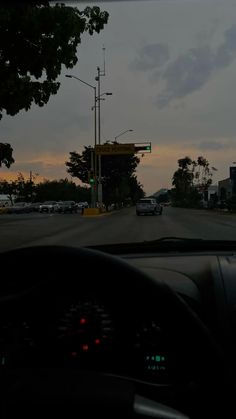 a car driving down a street next to a traffic light at dusk with the sun going down