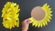 a person holding a piece of paper next to a sunflower cut out of cardboard