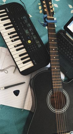 a guitar, keyboard and notebook on a bed