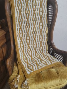 a crocheted blanket sitting on top of a wooden chair next to a wall