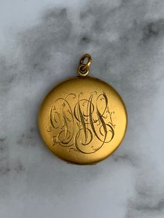 The vintage gold filled monogrammed locket exudes timeless elegance with its classic design and personalized touch. Crafted with precision and attention to detail, this exquisite piece features a sturdy gold filled construction, ensuring durability and a lustrous shine that will last for years to come. The locket showcases a vintage-inspired aesthetic, characterized by its ornate engravings and intricate detailing. The surface of the locket is adorned with a delicate monogram, adding a touch of personalization and making it a truly unique piece. Whether it bears your initials or someone dear to your heart, the monogram adds sentimental value and makes this locket the ultimate keepsake. With a hinge that opens smoothly and securely, the locket reveals two compartments to hold cherished phot Gold Medallion Locket Necklace Stamped 14k, Victorian Round Locket Necklace Stamped 14k, Antique Gold Locket Necklace Stamped 14k, Vintage 14k Gold Locket Necklace, Vintage 14k Gold Locket Necklace Stamped 14k, Vintage Gold Locket Necklace Stamped 14k, Vintage 14k Gold Locket Necklace With Vintage Charm, Victorian 14k Stamped Round Locket Necklace, 14k Gold Locket Necklace With Vintage Charm