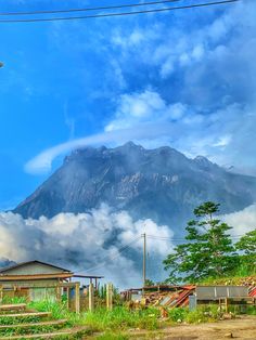 there is a mountain in the background with clouds coming up from it and houses below