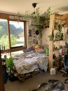 an unmade bed sitting next to a window in a room with lots of plants