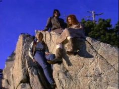 three people sitting on top of a large rock next to each other in the air