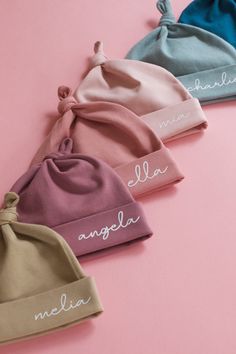 three beanies with names on them sitting next to each other in front of a pink background