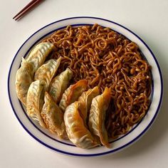 a white plate topped with dumplings and noodles next to chopsticks on a table