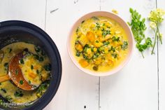 two bowls filled with soup next to each other on a white wooden table and green leaves