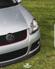 the front end of a silver car parked on top of a grass covered field next to a parking sign