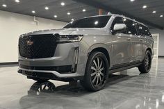 a silver suv is parked in a large room with white walls and lights on the ceiling