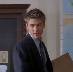 a young man wearing a suit and tie holding a box in front of his face