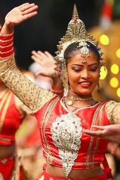 a woman in a red and gold outfit dancing with her hands out to the side