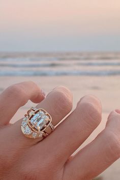 a person's hand with a ring on it and the ocean in the background