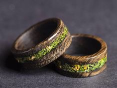 two wooden rings with moss and yellow flowers on them sitting on a table next to each other