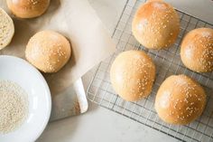 several buns with sesame seeds on a cooling rack next to a bowl of oatmeal