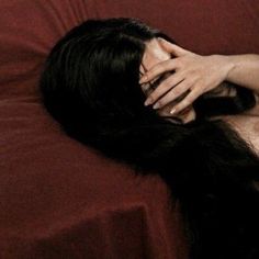 a woman laying on top of a red couch with her hands covering her face and head