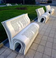 two white park benches sitting next to each other on top of a cement slab covered in grass