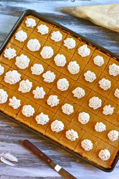 a pan filled with white frosted cookies on top of a wooden table next to a knife