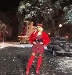 a woman in a red coat and plaid skirt standing next to an old fashioned car