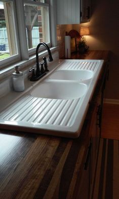 a kitchen sink sitting under a window in front of a counter top with two faucets