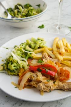 a white plate topped with meat and veggies next to a glass of wine