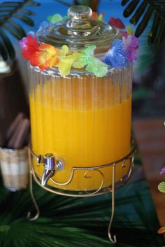 a glass filled with orange juice on top of a metal stand next to some flowers