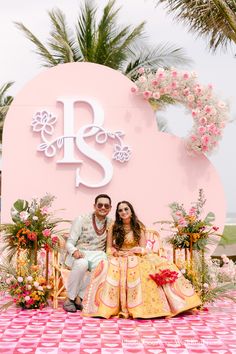 a man and woman sitting on a bench in front of a pink sign with flowers