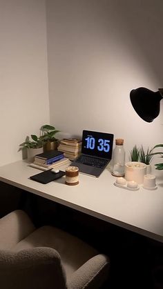 a laptop computer sitting on top of a white desk next to a lamp and books