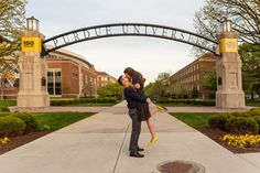 a man holding a woman in front of an arch with the words university on it