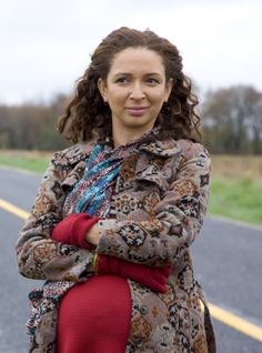 a woman is standing on the side of the road with her arms crossed and looking at the camera