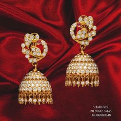 pair of gold plated jhuma earrings with white stones and pearls on red silk background