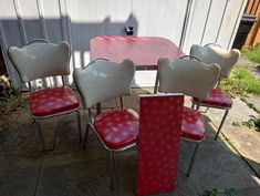 four chairs with red and white cushions are around a small table in front of a house