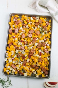 a pan filled with sausage and vegetables on top of a white table next to an apple slice