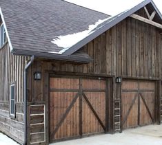 an old barn with wooden doors and snow on the roof