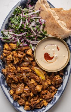 a blue and white plate topped with meat, salad and pita bread